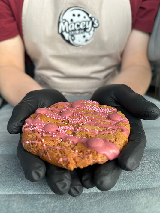 Een vrolijke traktatie met een verrassende twist! Deze chewy cookie is rijk gevuld met romige roze chocoladedruppels &nbsp;“onze pinklets” en afgewerkt met een swirl van roze chocolade en knapperige pareltjes. De smaak? Een zoet-romige mix met een vleugje citroenzuur en extra vanille-extract voor die volle smaakbeleving. Perfect als je zin hebt in iets anders dan gewoon zoet.
